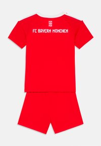 Crvena sportska oprema FC Bayern Münchena koja se sastoji od majice kratkih rukava s bijelim naglascima i logotipom, uparenih s odgovarajućim crvenim hlačicama.