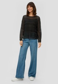 Top nero trasparente a maniche lunghe con strisce orizzontali, abbinato a jeans a gamba larga blu chiaro e sneakers bianche con platform.