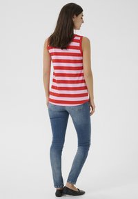Haut sans manches rayé rouge et rose avec un col rond, associé à un jean skinny délavé moyen et des chaussures plates noires.