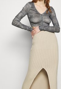 Grauer Cropped-Top mit einem strukturierten Muster, lange Ärmel und V-Ausschnitt. Darunter ein beiger, gerippter Rock mit einem seitlichen Schlitz.