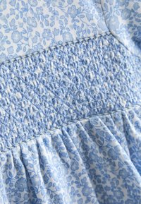 Tessuto floreale blu e bianco con ricamo smock blu dettagliato e cuciture arricciate su una sezione del capo.