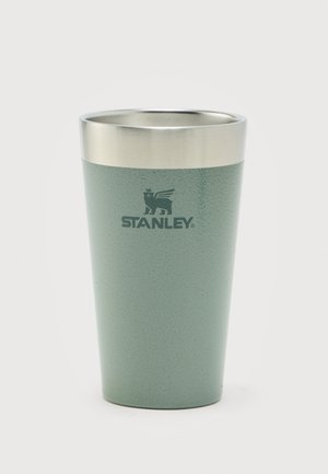 Vaso metálico aislante verde Stanley con borde plateado y logo de león alado en el frente, colocado sobre fondo blanco.