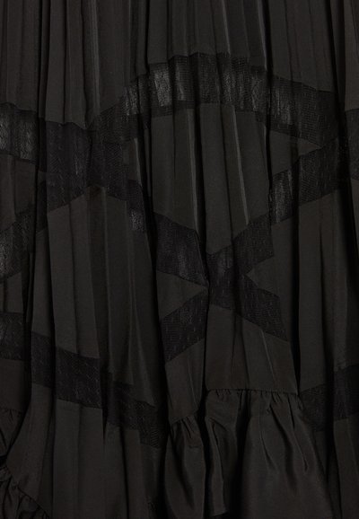Zwarte geplooide rok met contrasterende doorzichtige en gestructureerde zwarte stoffen panelen, featuring een gerimpelde zoom en geometrische patronen in een gestructureerd ontwerp.