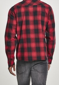 Röd och svart rutmönstrad skjorta med knappkrage, långa ärmar och rak fåll. Tillverkad i bomull med en mjuk textur, bärs tillsammans med grå jeans.