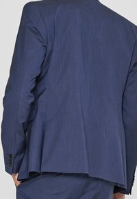 Marinblå kostymjacka i strukturerad tyg, med en slits, kammade slag och fyra knappar vid ärmsluten.