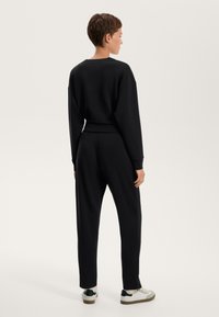 Set di felpa e pantaloni neri, con una vestibilità comoda e polsini a costine. Il tessuto ha una consistenza liscia, indossato con sneaker bianche.