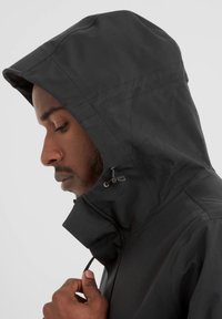 Black hooded jacket with a high collar, made of smooth fabric. Features adjustable drawstring and a sleek design, viewed from the side.