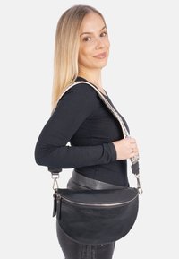 Schwarze Lederhandtasche mit einer geschwungenen Form, Reißverschluss, strukturierter Oberfläche und einem gemusterten, verstellbaren Riemen.
