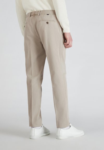 Beige katoenen broeken met een rechte snit, achterzakken en knoopdetails. Gepaard met witte sneakers en lichte sokaccenten.