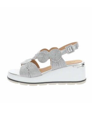 Sandale compensée argentée avec brides circulaires tressées et boucle à la cheville sur une semelle plateforme blanche.