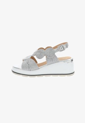 Sandalo con zeppa argento con cinturini intrecciati a cerchio e fibbia alla caviglia su suola platform bianca.