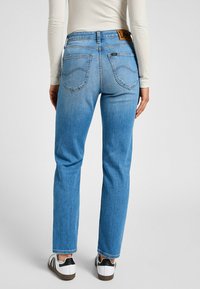 Jeans de mezclilla azul con un corte recto, que presentan una etiqueta de cuero marrón en la cintura y costuras en contraste en los bolsillos.