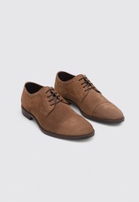 Braune Wildleder Schnürschuhe mit einem Kapuzenspitze-Design, das über perforierte Details entlang der Kanten verfügt und eine flache Gummisohle hat.