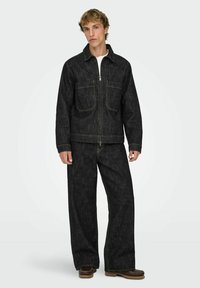 Tume teksatagi ja laiade pükstega püksid, kollaste õmblustega, kahe eest tasku ja lukuga sulgemisega. Sile tekstuur ja keha järgnev lõige.