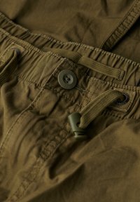 Olijfgroene katoenen shorts met een elastische tailleband, trekkoord en een knoopsluiting. Kenmerkt zich door stiksels en een gestructureerde stof.