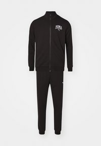 Completo sportivo nero realizzato in tessuto morbido; include una giacca con zip e colletto alto, polsini a costine, abbinata a pantaloni a sigaretta con un accento del logo.