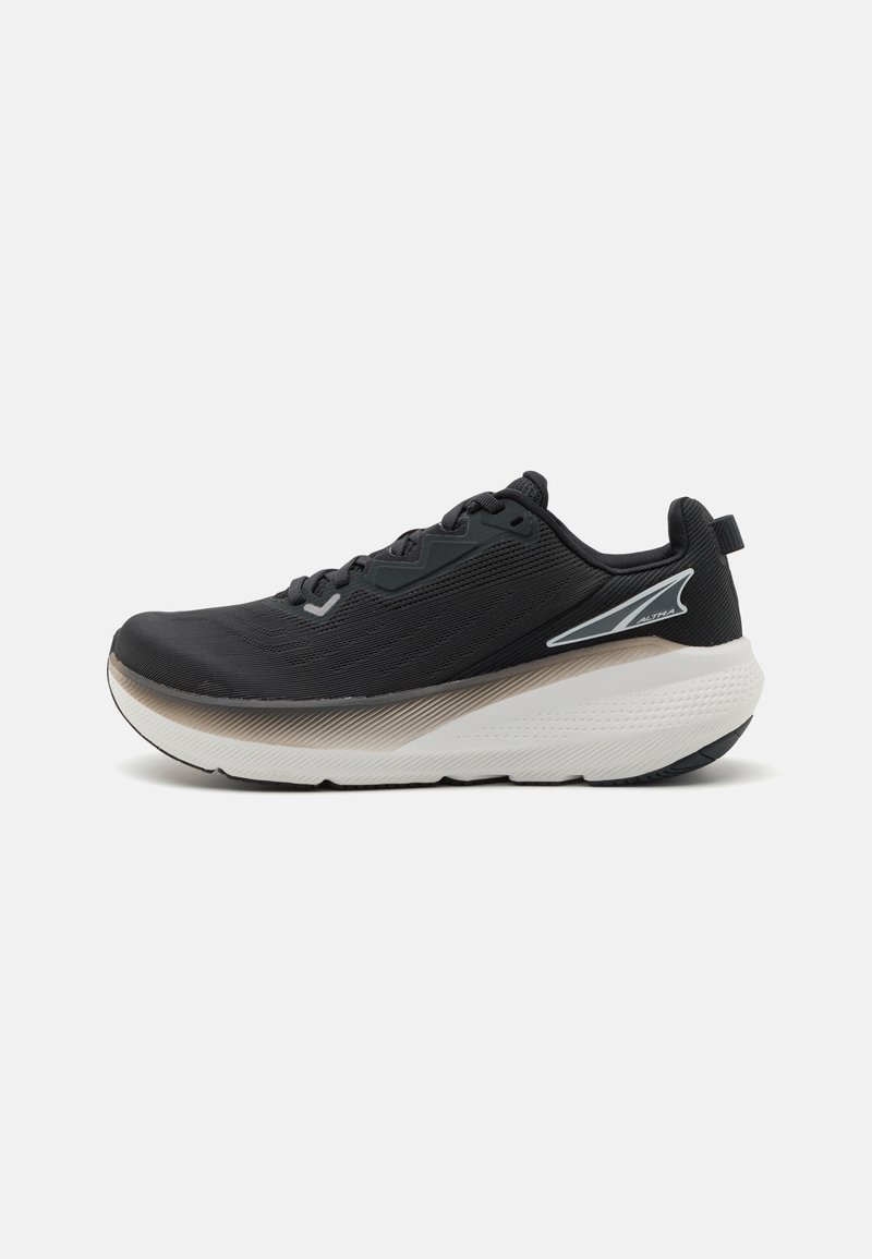Chaussure de sport noire avec une tige texturée, semelle blanche et beige, bout rond et accents minimalistes comprenant un détail réfléchissant sur le côté.