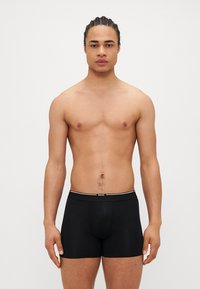 Schwarze Boxershorts aus einem weichen Stoff mit einem weißen, markierten Bund. Das Design ist figurbetont und bietet Unterstützung sowie Komfort.