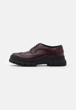Buty brogue z ciemnego bordo skóry, z czarną masywną gumową podeszwą i zapięciem na sznurowadła, przedstawione z profilu na białym tle.