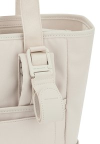 Jasno beżowa torba na ramię z teksturowanej tkaniny, z gładkim paskiem i plastikowym zapięciem. Widoczne przeszycia na krawędziach.