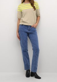 Beige kortærmet sweater med fluorescerende gule striber, parret med blå lige ben jeans og sorte, chunky hæle ankelstøvler.