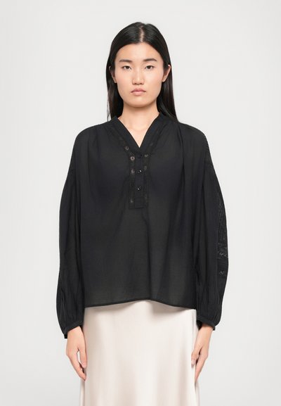 Blouse noire avec un décolleté en V, patte de boutonnage et accents en dentelle sur les manches. Tissu léger avec une coupe décontractée, manches légèrement bouffantes.