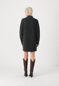 Vestido de malha cinza escuro com um decote alto, mangas longas e uma silhueta ajustada, combinado com botas de cowboy castanhas com um bico pontiagudo.