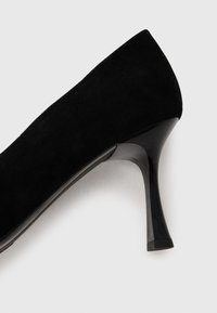 Black suede high heel shoe with a pointed toe and shiny black heel. The texture is smooth and fabric appears soft.