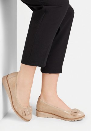 Beżowe baleriny o fakturowanym wykończeniu, z kokardką na palcu oraz niską, rowkowaną podeszwą. Połączone z czarnymi spodniami 3/4.