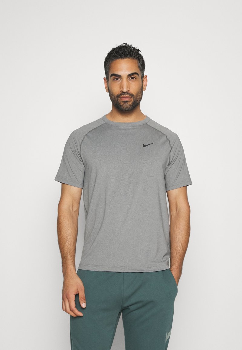 Grå atletisk t-skjorte med korte ermer, rund hals, og svart Nike-logo på brystet. Laget av pustende materiale med en jevn tekstur.