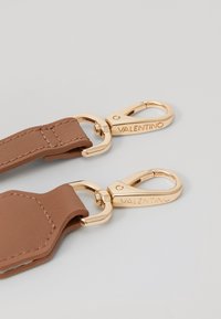 Hnědý kožený řemínek se zlatými kovovými přezkami, zdobený vyraženým logem "VALENTINO" a texturovaným povrchem.