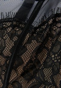 Svart spetsunderkläder med intrikata blommönster över en beige bas, med fin mesh och kontrasterande strukturella detaljer.