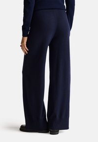 Pantaloni a gamba larga di colore blu navy realizzati in un tessuto morbido, con vita e polsini a costine, caratterizzati da una superficie liscia e una vestibilità rilassata.