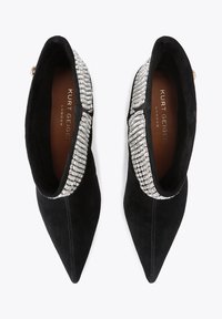 Zwarte suède schoenen met een puntige neus en een sprankelende kristallen versiering rond de enkel. De binnenvoering toont "Kurt Geiger London."