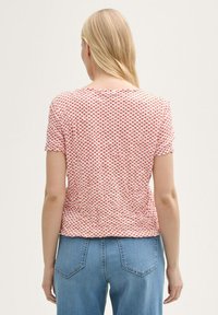 Haut à manches courtes rouge et blanc à motifs, avec un col rond et un tissu texturé, associé à un jean taille haute bleu clair.