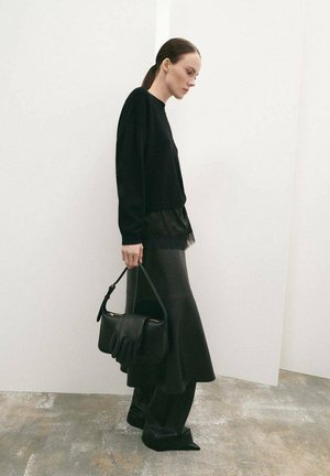 Crna skraćena majica slojevito preko crne suknje s čipkastim rubom, uparena sa strukturiranom crnom torbom sa valovitim dizajnom.