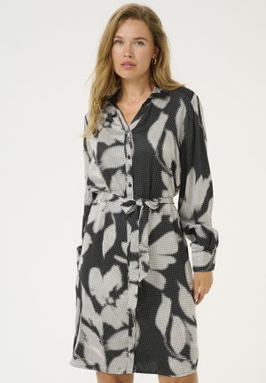 Robe noire et blanche à boutons avec un motif floral, texture de tissu, manches longues, ceinture à nouer et poches latérales.