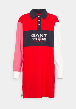 Maillot de rugby rouge à manches longues avec une manche gauche rose, une manche droite blanche, un col marine et un logo GANT 1949 sur une bande poitrine marine.