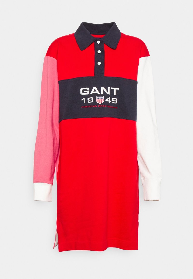 Maillot de rugby rouge à manches longues avec une manche gauche rose, une manche droite blanche, un col marine et un logo GANT 1949 sur une bande poitrine marine.