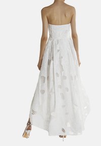 Hvid, strapless kjole med præget blomstermønster og udskæringsdetaljer. Den flydende nederdel strækker sig til gulvet og er parret med sølvfarvede hæle.