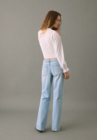 Vit strukturerad långärmad topp matchad med ljusblå högmidjade raka jeans. Detaljer inkluderar en kortad passform och resårmidja.