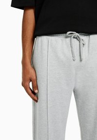 Grijze sweatpants met een trekkoord in de taille, zachte textuur, zijzakken, en zijnaad-details, gedragen met een zwart T-shirt met korte mouwen.