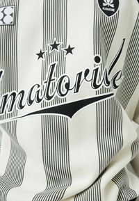 Camiseta blanca con finas rayas verticales negras, con el texto en negrita "Imatorive", tres estrellas y un logo en la esquina superior.
