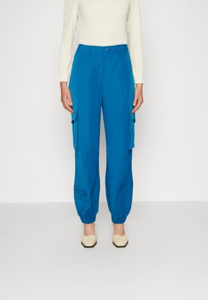 Μπλε cargo παντελόνι με ελαστικούς ιερείς στο τελείωμα, πολλαπλές πλαϊνές τσέπες και φερμουάρ. Κατασκευασμένο από απαλό, ελαφρύ ύφασμα.