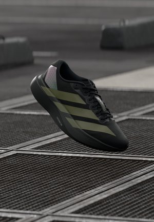 Chaussure de sport noire avec trois bandes vert olive, tige noire texturée et un accent motif rose et bleu au niveau du talon.