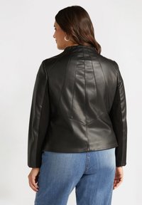 Black leather jacket with structured seams and a high collar, paired with blue denim. Smooth texture, fitted design, and long sleeves.
