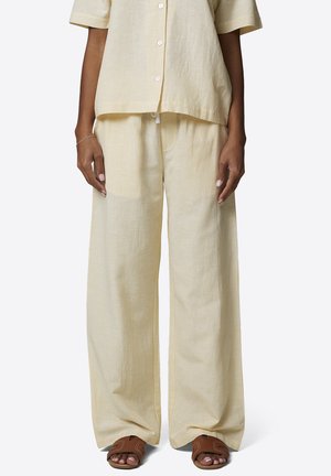 Femme portant un pantalon ample beige à rayures avec un haut boutonné à manches courtes assorti, associé à des sandales marron à bout ouvert.