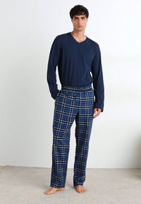 Top de culoare navy cu mânecă lungă și decolteu în V, asociat cu pantaloni din flanel cu carouri albastre și accente albe și negre, cu un croi lejer și talie cu șnur.