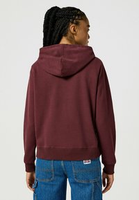 Bordeaux hoodie met een ruime capuchon, ribgebreide boorden en zoom, met een zachte textuur. Draag het met hoge taille blauwe jeans, met zichtbare naden.