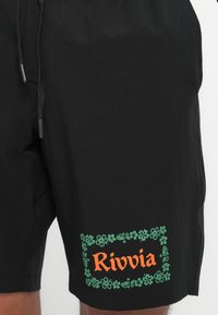 Čierne plavky s elastickým pásom, so šnúrkou a zeleným kvetinovým logom s nápisom "Rivvia" v oranžovej na ľavej strane.